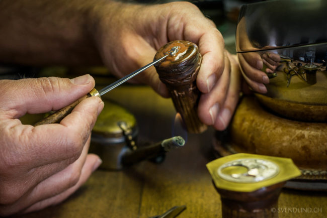 An artisan prepares a watch component before engraving it.