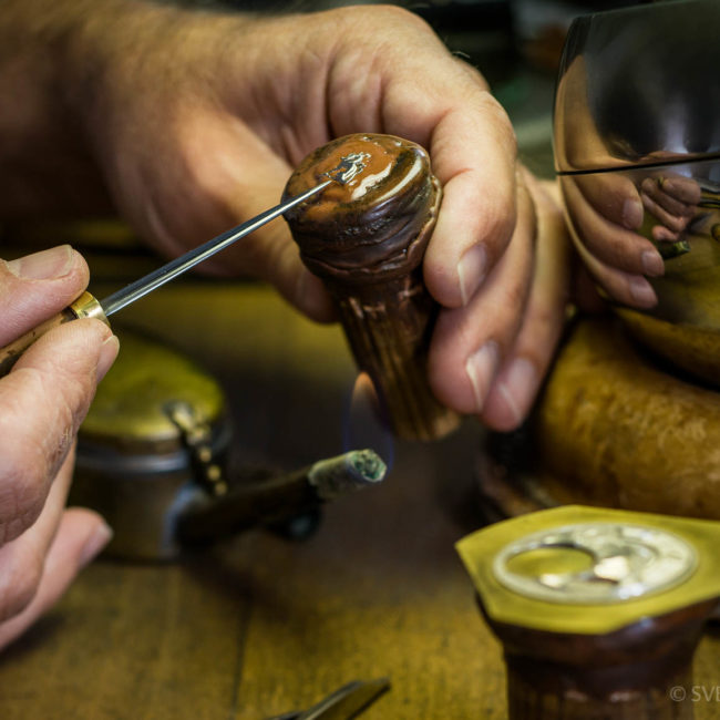 An artisan prepares a watch component before engraving it.