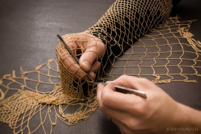 An artisan works on a gold chain mesh.