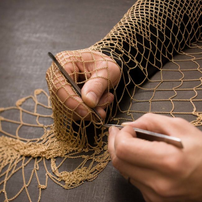 An artisan works on a gold chain mesh.