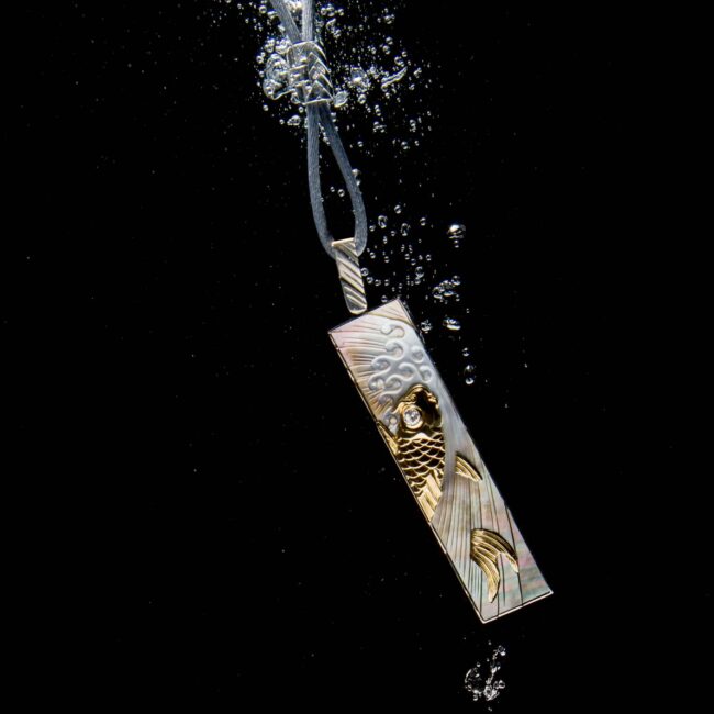 Engraved mother of pearl & diamond catfish pendant necklace underwater.