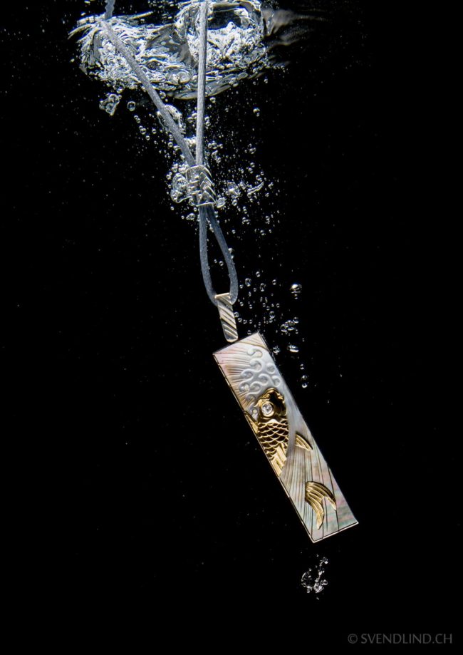 Engraved mother of pearl & diamond catfish pendant necklace underwater.